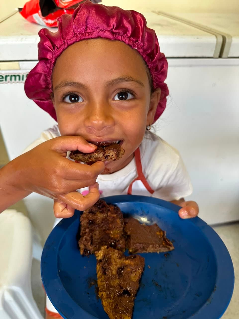 Crianca meninina comendo uma panqueca com touca vermelha na cabeça